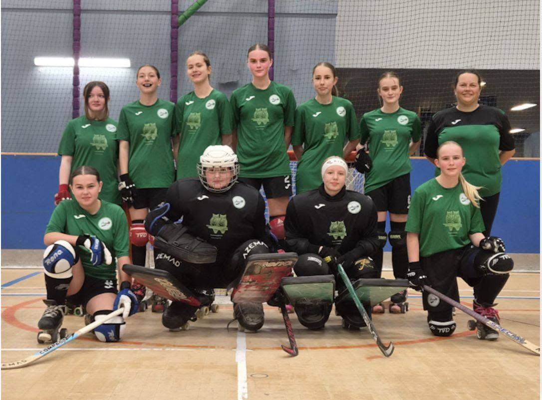 A girls squad lined up with sticks in front of the goal
